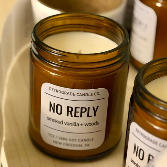 Brown glass jars with white candles labeled 'No Reply' on a wooden surface.